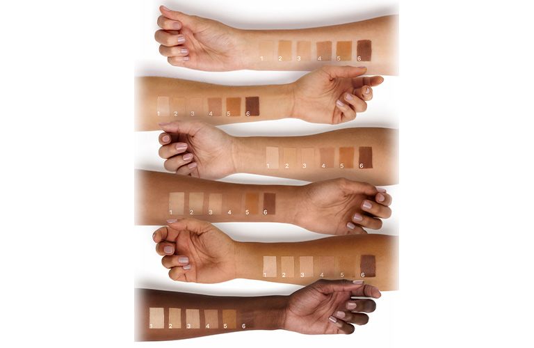 Foto con fondo blanco, muestra varios antebrazos de distintos tonos de piel alineados horizontalmente, cada uno con muestras numeradas de base de maquillaje aplicadas sobre la piel.